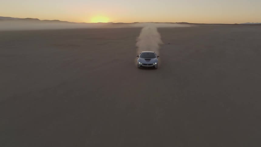 A gray sports car is driving across a flat desert