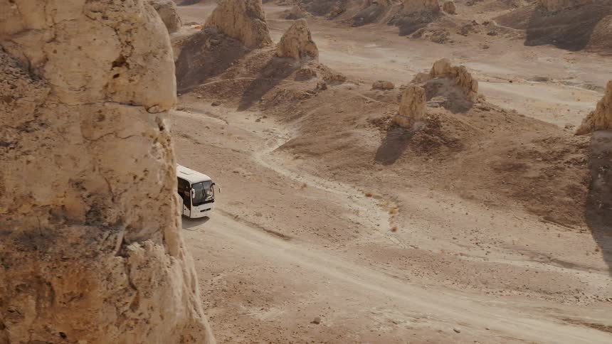 A bus driving on a dirt road in the desert next to mounds