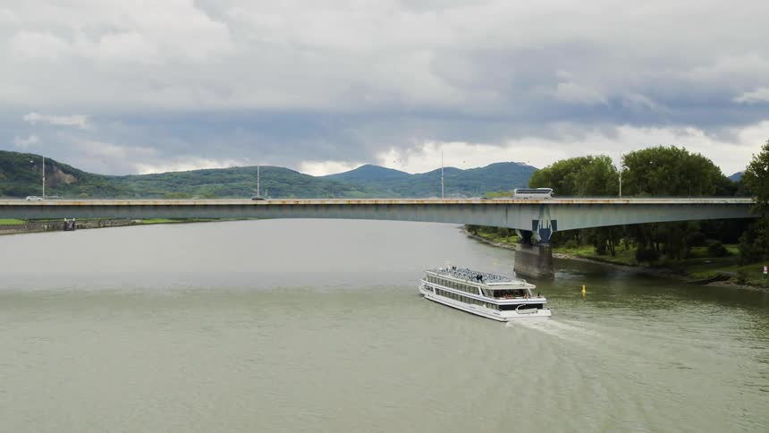 Aerial view of a white ferry passing under a bridge on a cloudy day