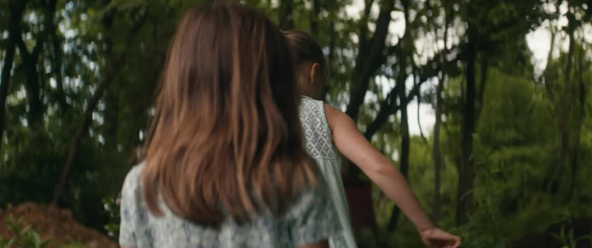 Mother with a blue hat and a white shirt and daughters with a blue blouse and shift walk on a track in the woods
