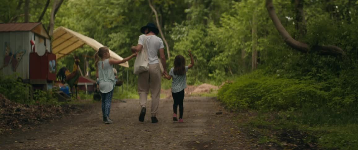 A woman walks with two young girls down a dirt path through a forest