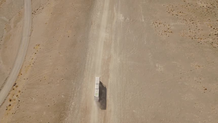 Vehicle follows dirt road through desert kicking up dust