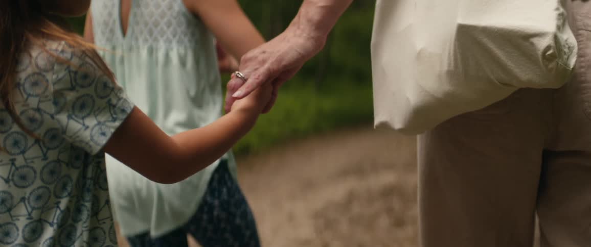 An old woman holds a childs hand as they walk down a dirt path