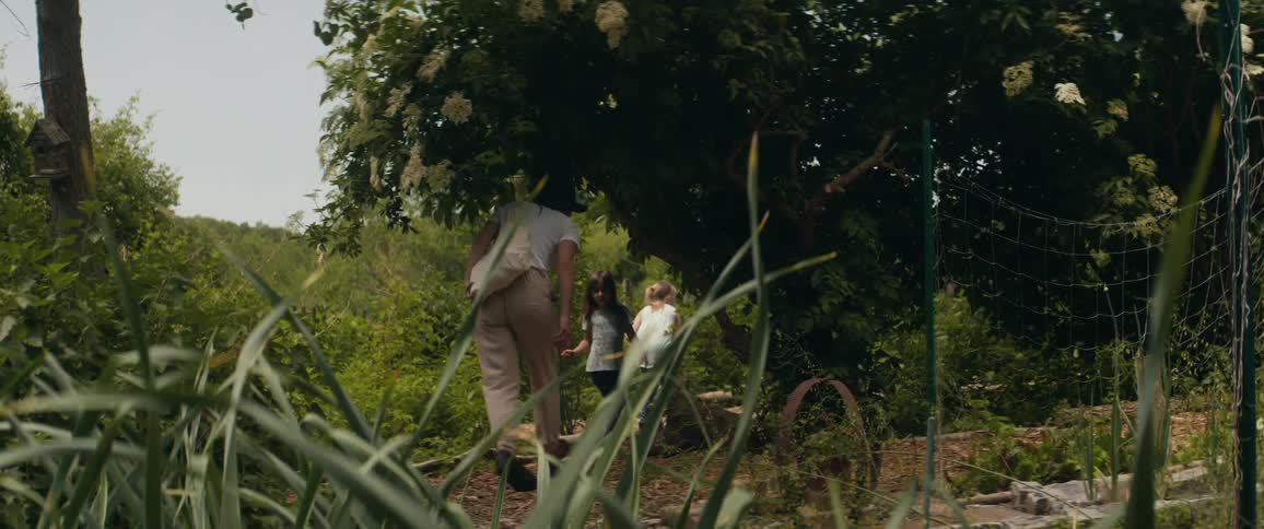 An older white woman walks over to two children in a garden
