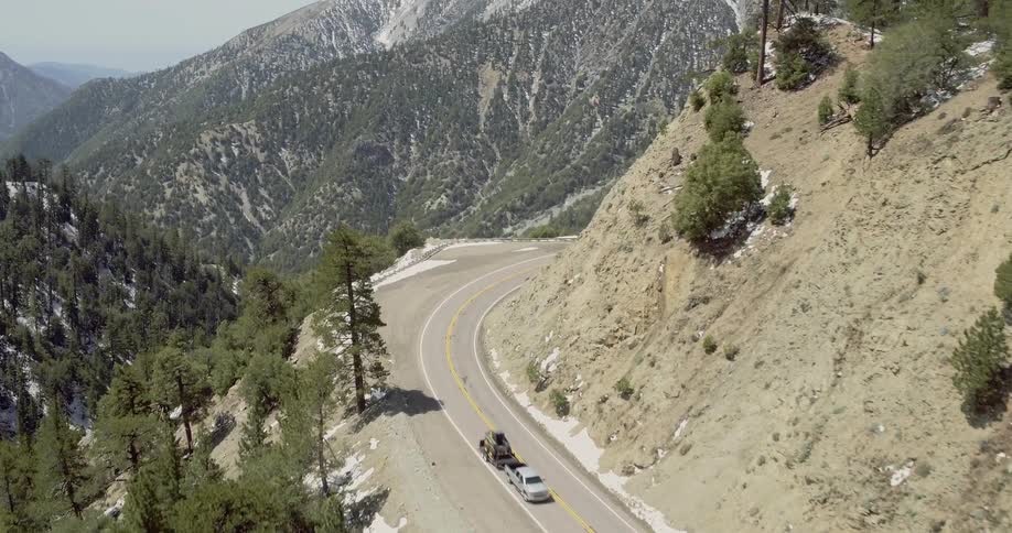 Pickup truck pulls a trailer with a vehicle on it on a road near the mountains