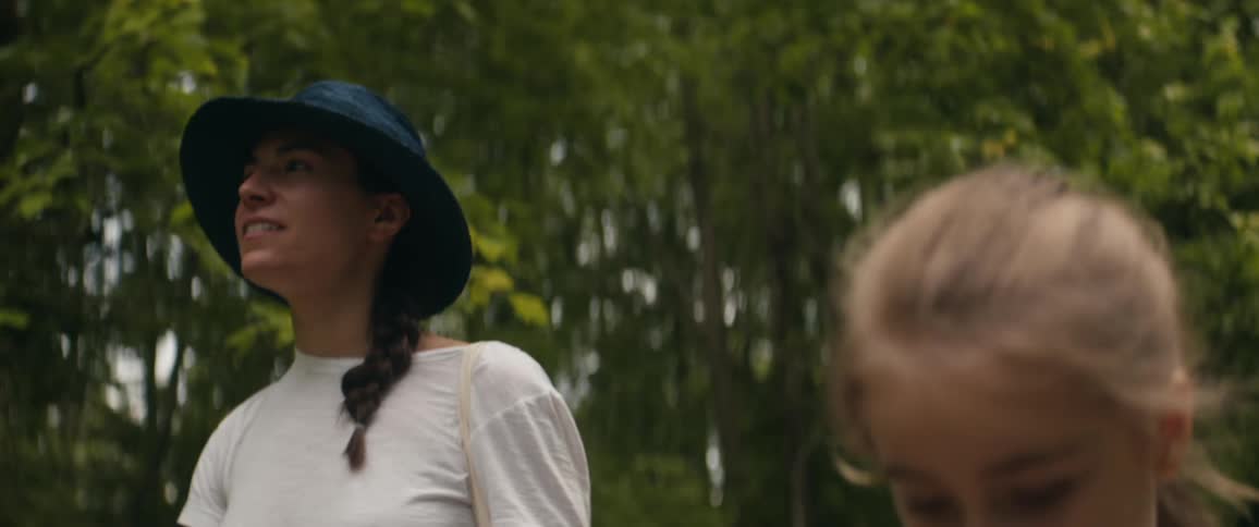 Happy mother with a blue hat and a white shirt and blonde daughter walk in the woods