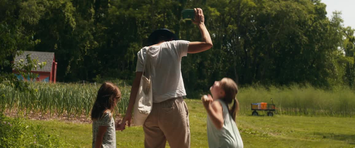 Mother and daughters walk across lawn near crop field playing