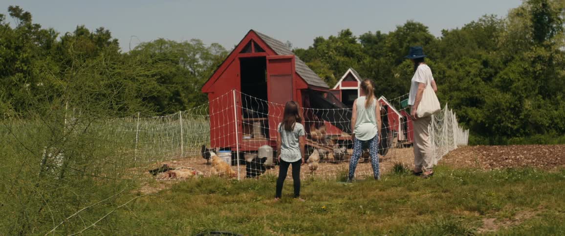A woman and her two daughters check on chickens in a red chicken coop