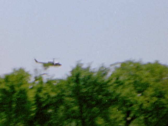Helicopter flies over the tree lines near a building