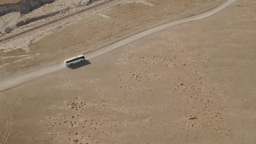 Aerial shot of a bus driving down a dirt path in the desert