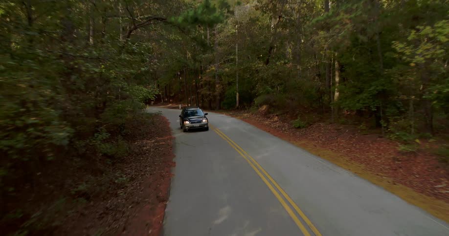 Aerial view of a black car drives on a highway through a forest