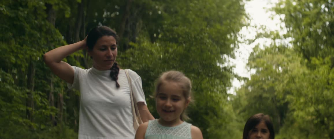 Mother and two young daughters walk in the forest while one child removes a hat from the mother and puts it on her head