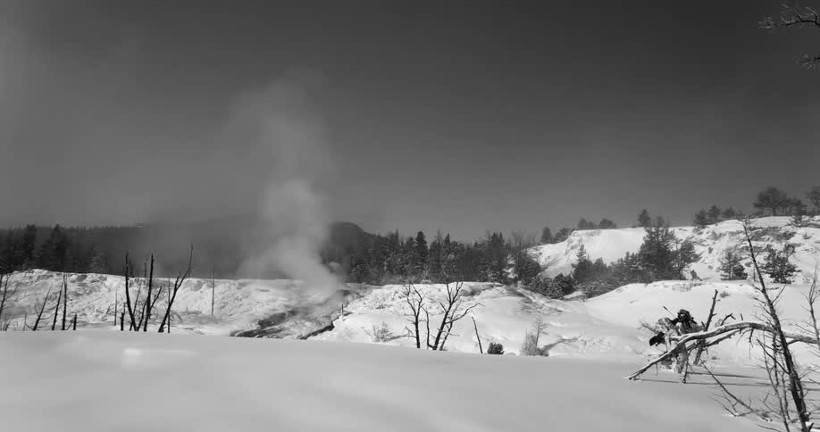 Man carrying video camera on tripod walks across snow drift