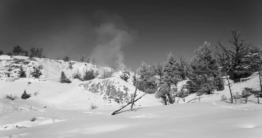 Man wearing winter clothes carry equipment through the snow covered hills near a natural steam vent