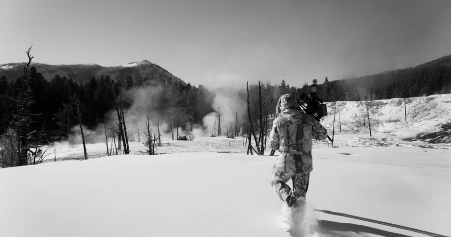 Photographer carrying a camera trekking through fresh snow towards a hot spring