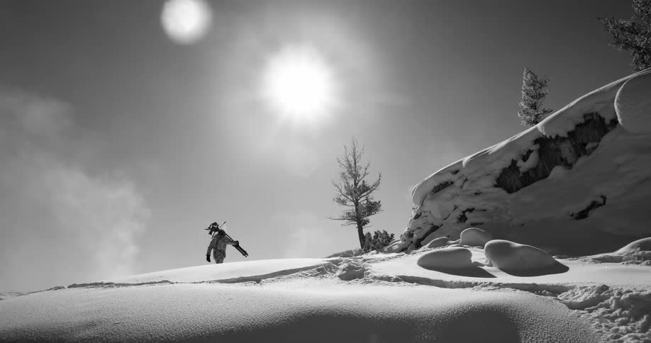 A photographer hikes through snow with a camera and tripod hoisted over his shoulder