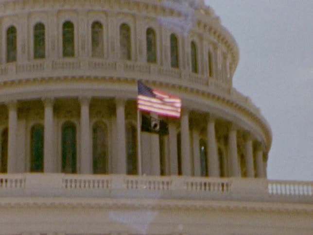 An american flag flies in front of the dome of a capitol building