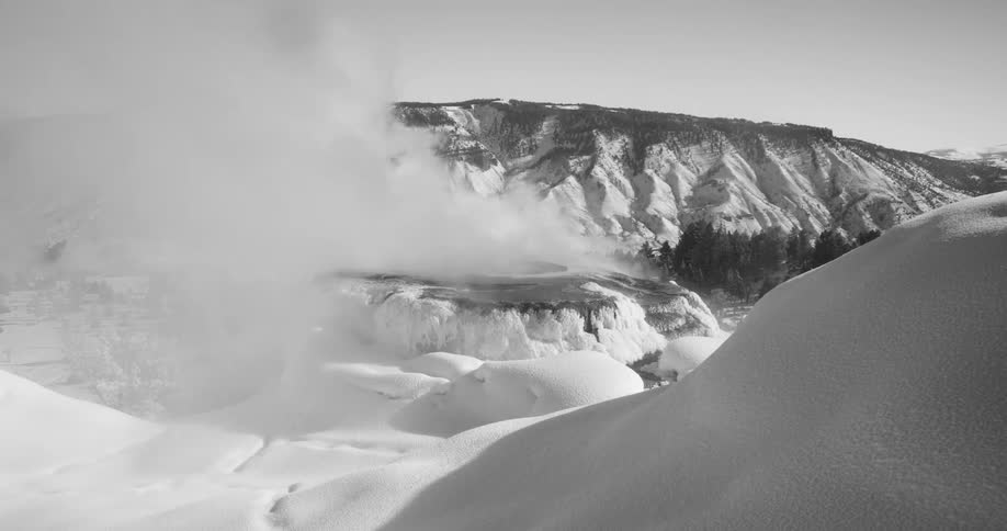 Steam and fog rise and billow over snow covered hills and peaks