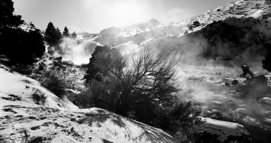 Hiker walks down the snowy side of a mountain while carrying a camera mounted on a tripod
