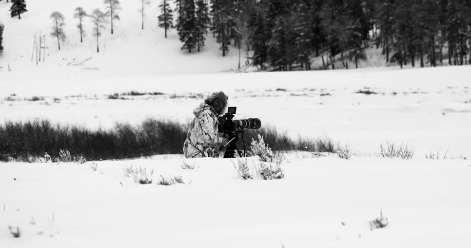 Photographer in winter gear stands in the snow with camera near the trees