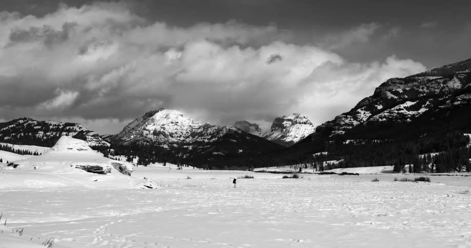 Hiker walks through snow covered field in front of mountains