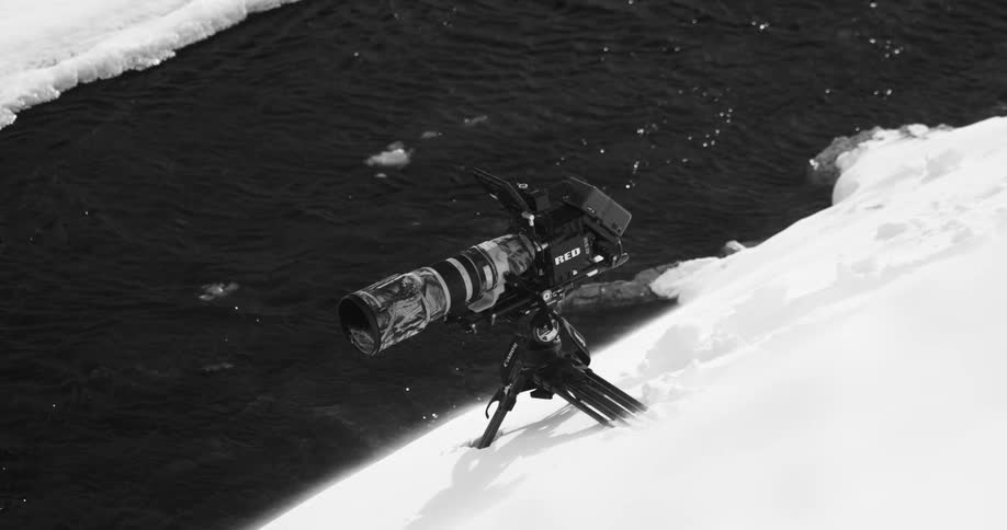 Photography camera on a tripod over the snow on the river bank