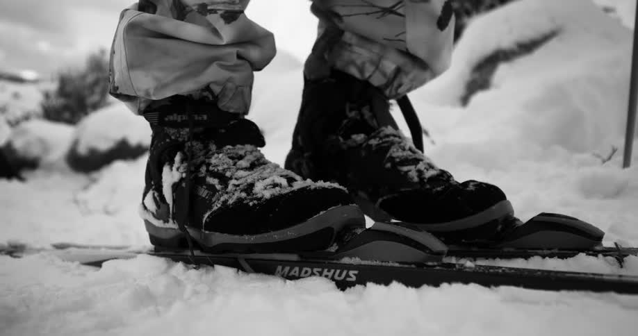 Man in winter gear puts on skis on the snow outdoors