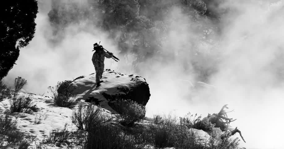 A person with a camera and a tripod walking on a cliff next to smoke