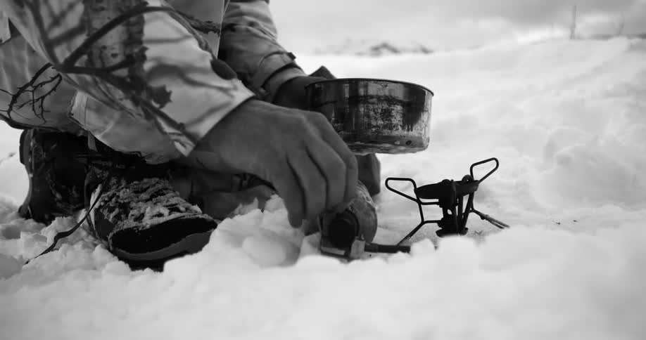 A person attempts to light a campfire stove in deep wilderness snow