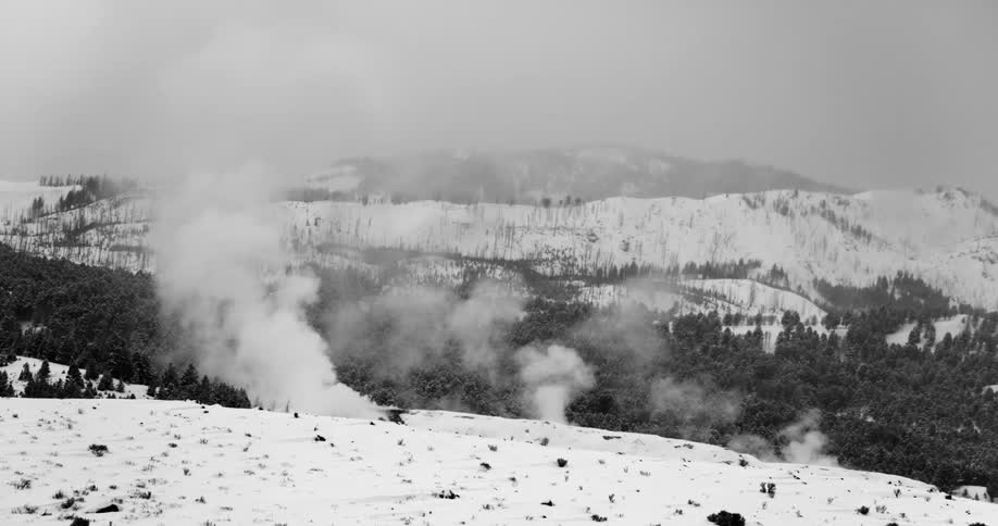 A snowy field with smoke and trees with the sky and mountains in the background