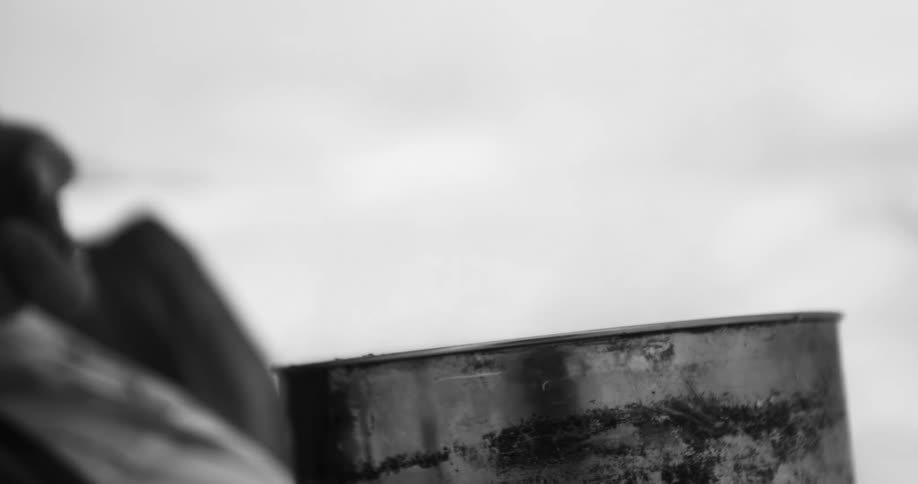 A gloved hand fidgets while steam rises from a cooking pot outdoors