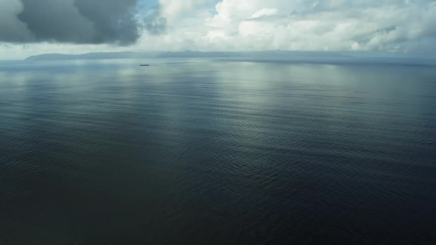 Heavy clouds reflect off ocean waters as ship passes parallel to distant shoreline