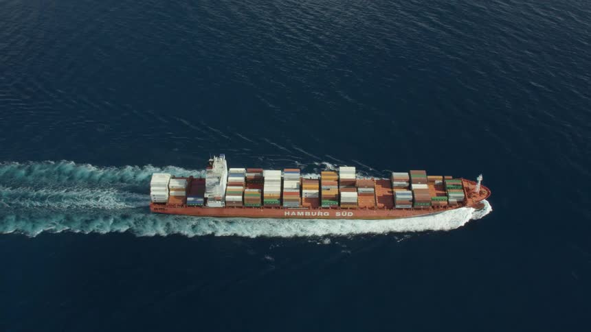 Container ship moves across dark rippling water leaving a white water wake