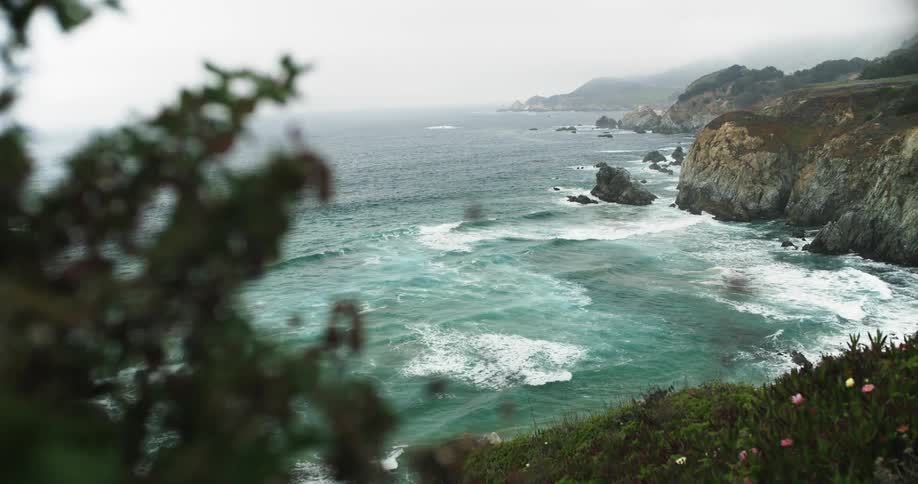 Ocean waves crash against oceanside cliffs on a cloudy day
