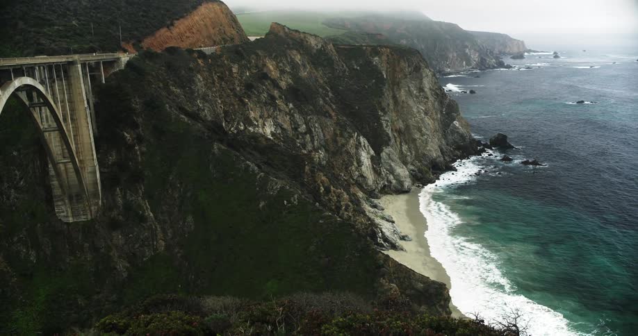 Traffic crosses sturdy bridge standing near cliff bordering ocean