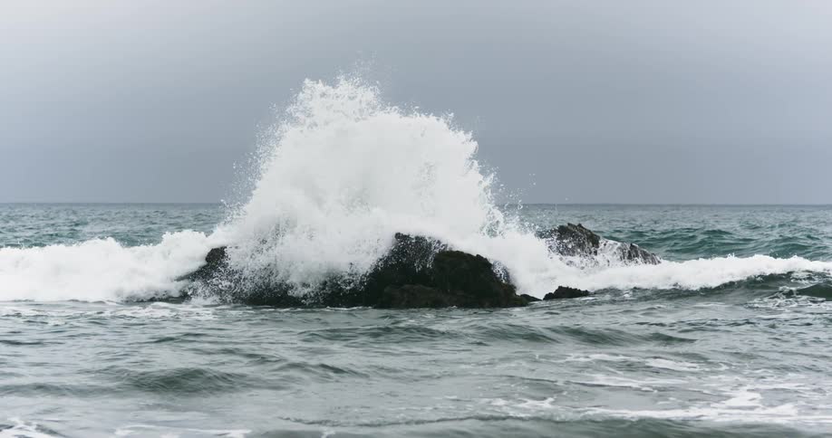 Ocean waves crashing on the black rocks near the coast