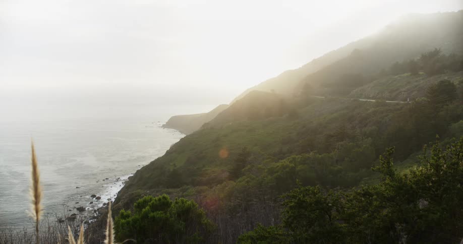 Sunlight filters through the clouds over the mountains near the ocean