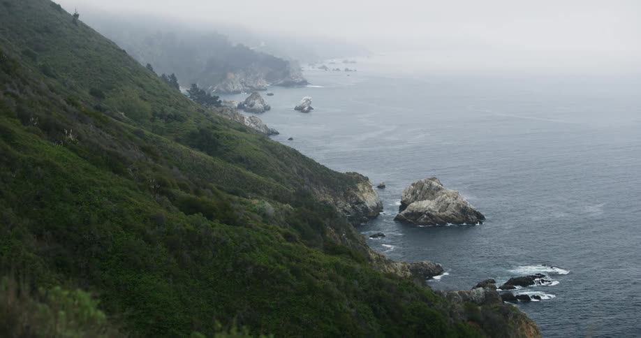 Ocean waves crash on the rocks of coastal cliffs under the fog
