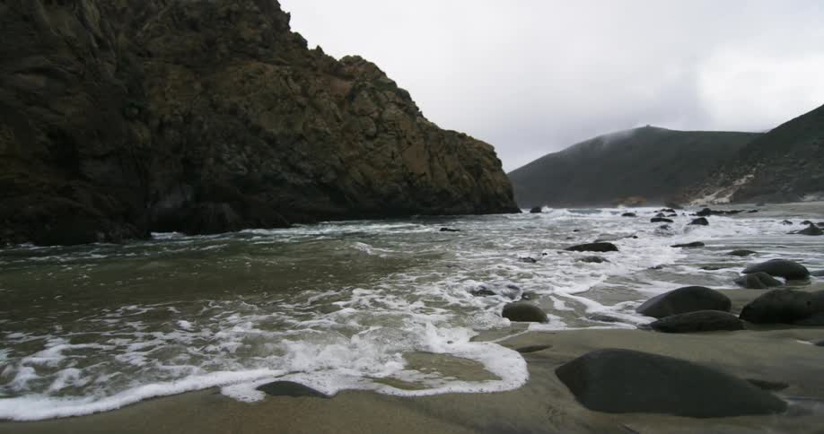 Ocean waves gently crashing on the black rocks of a beach in front of a promontory