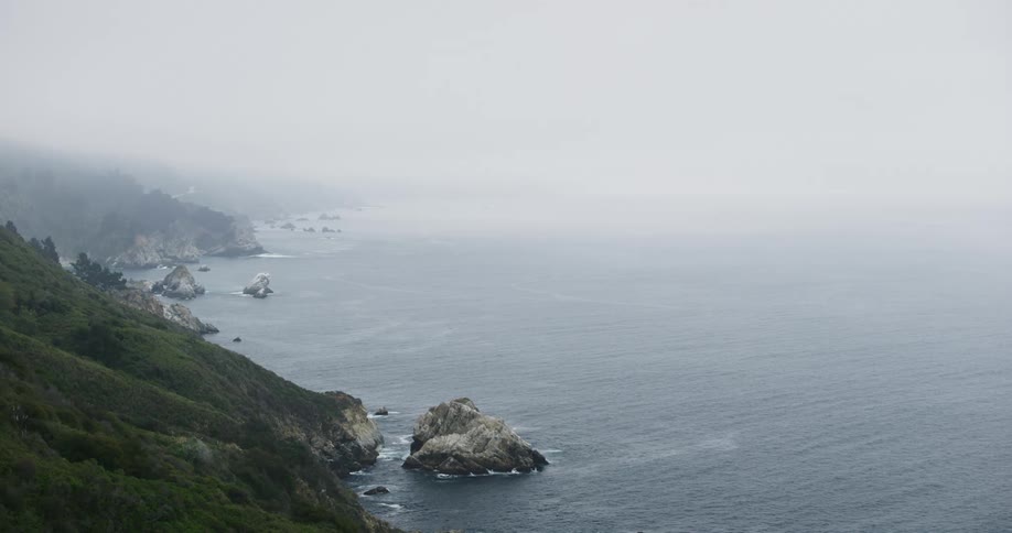 Ocean waves roll in towards the rocks next to the hilly land