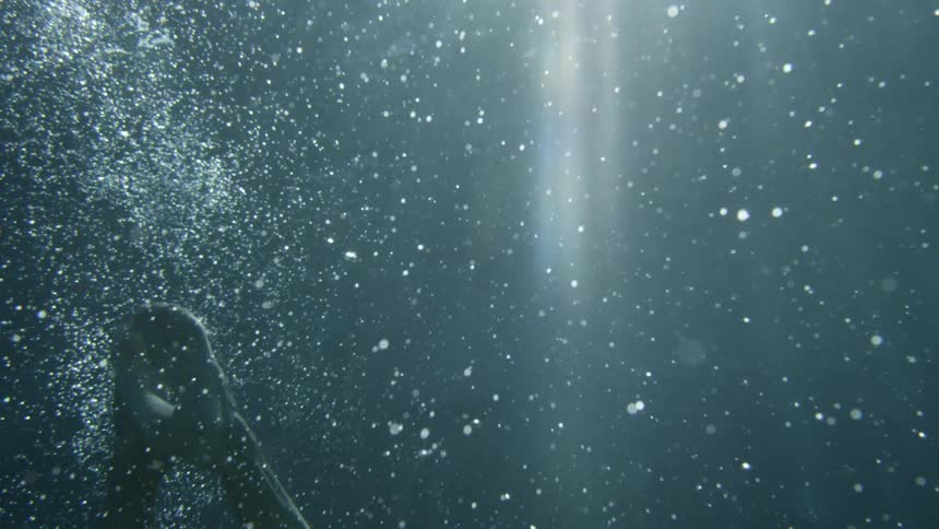 Person sinks down underwater forming bubbles as suns rays shine through