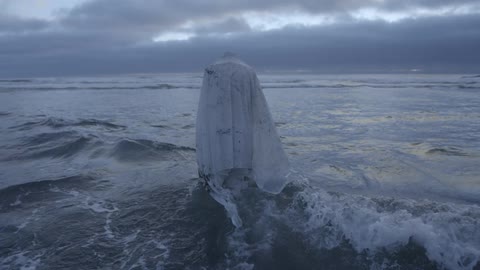A person wrapped in a large white cloth walks into the ocean