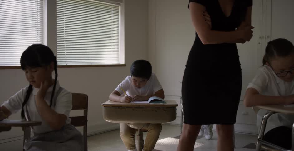 Boys and girls studying in a classroom while the teacher walks around the desks