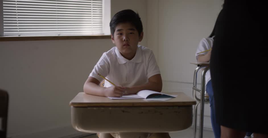Young asian boy sitting at a desk in school takes notes on a notebook with a pencil