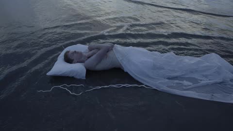 Man laying down on sand in ocean water with tarp