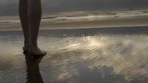 A person is walking towards the water at sunset
