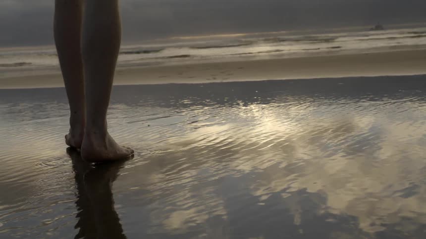 A person is walking towards the water at sunset