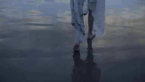 A person wrapped in a white sheet walking along wet sand on a beach