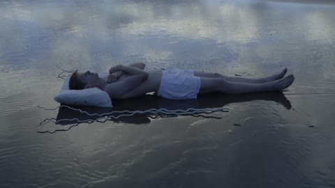 A man's body is uncovered from a sheet on the beach
