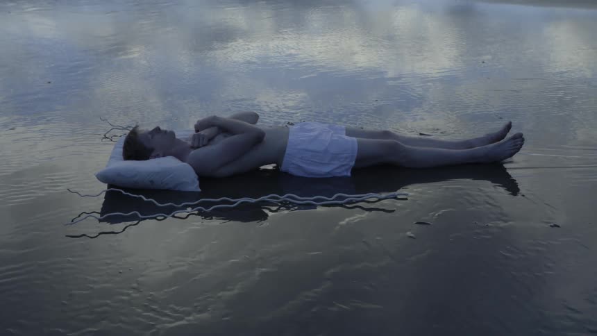 A man's body is uncovered from a sheet on the beach